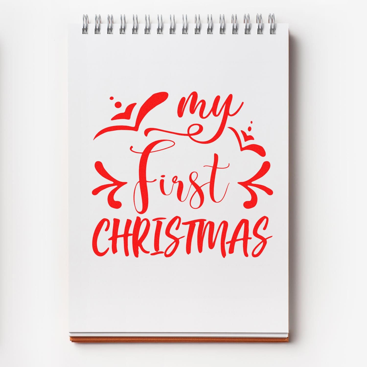 Red my first Christmas custom stamp design on a white spiral notepad with festive script and decorative flourishes.
