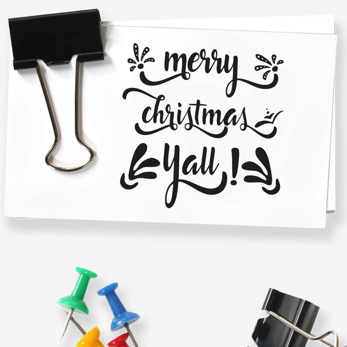 Black Merry Christmas Yall stamp with decorative flourishes, plus binder clip and colorful seal pushpins.