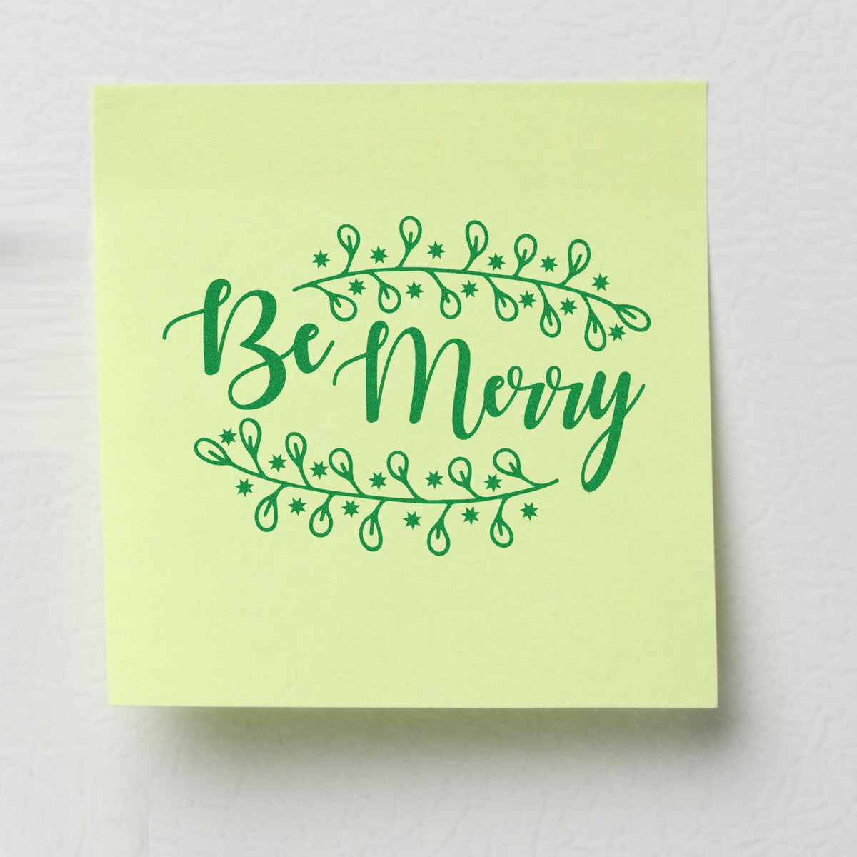 Green Be Merry holiday stamp and seal on pale yellow square note, framed by string lights and stars.