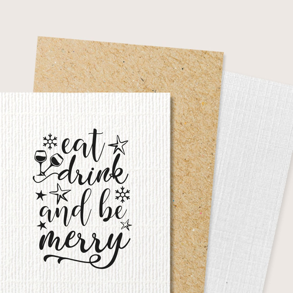 Black holiday stamp and seal design reading eat drink and be merry on white textured card with stars, snowflakes and wine glasses.