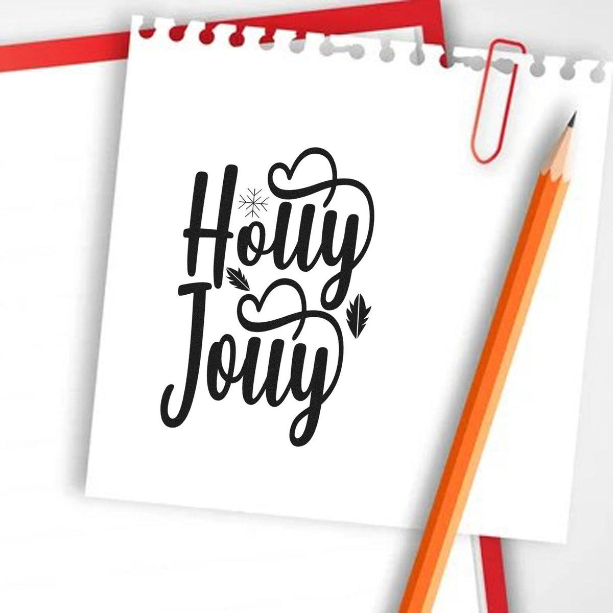 Black Holly Jolly stamp design on white paper, with red paperclip and orange pencil for festive seal products.