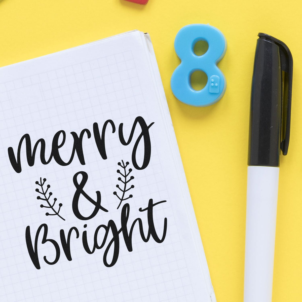 Black merry & bright lettering on white grid paper, with a blue number 8 stamp/seal and black-and-white seal pen on yellow background.