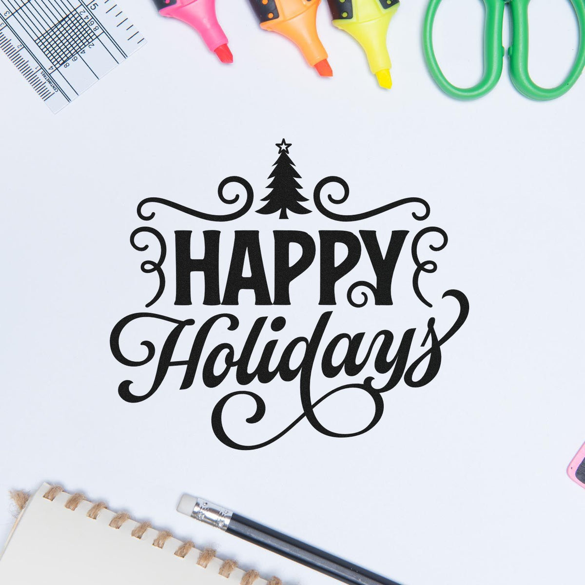 Black Happy Holidays decorative stamp seal with Christmas tree flourish, surrounded by neon markers, green scissors, ruler and pencil.
