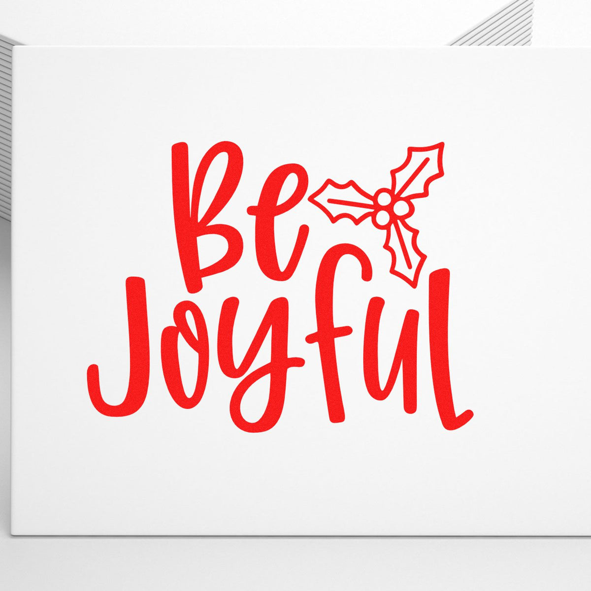 Red "be joyful" holiday stamp/seal design with holly accent on white background for festive branding.