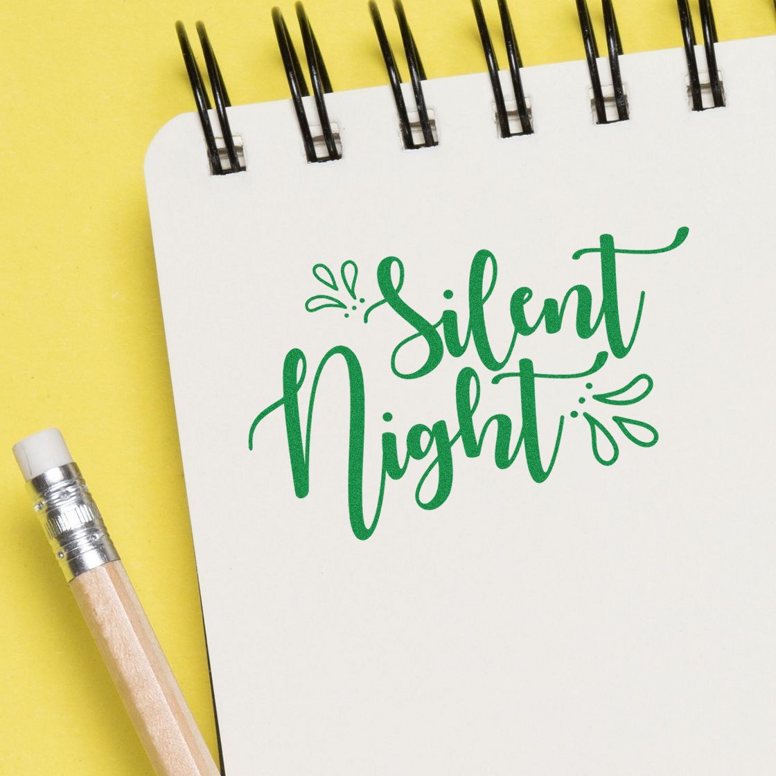 Green Silent Night stamp and seal design on a white spiral notebook, with a pencil on a bright yellow background.