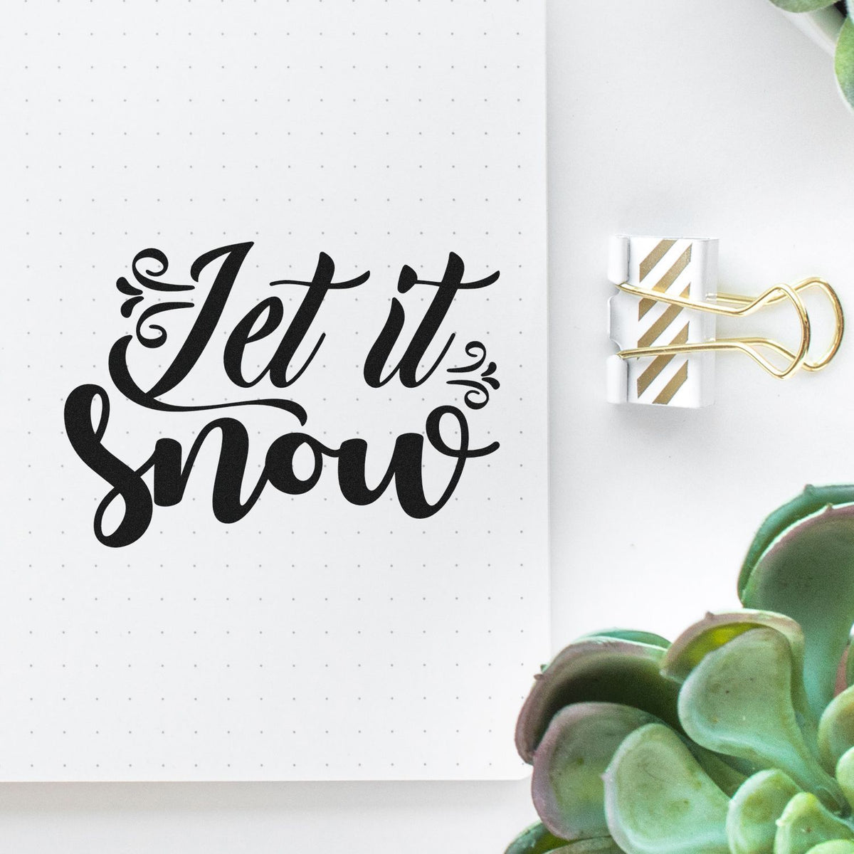 Black Let it snow stamp on dotted planner page beside white-and-gold striped seal tape.