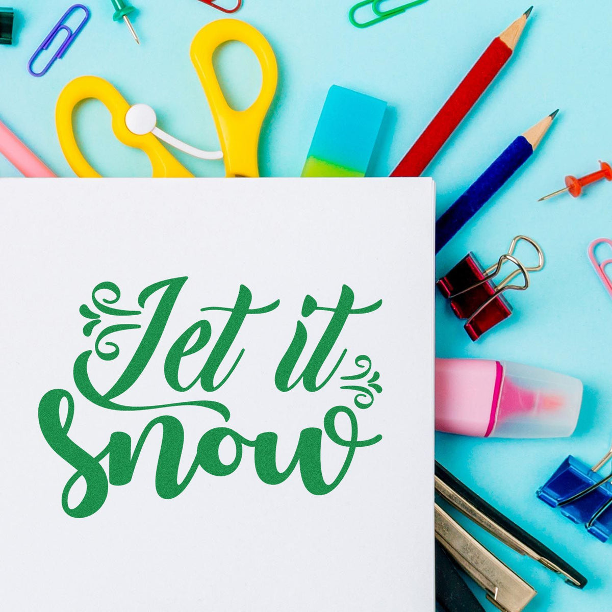 Green Jet it snow stamp and seal on white card, with colorful stationery, yellow scissors, pencils, and binder clips.