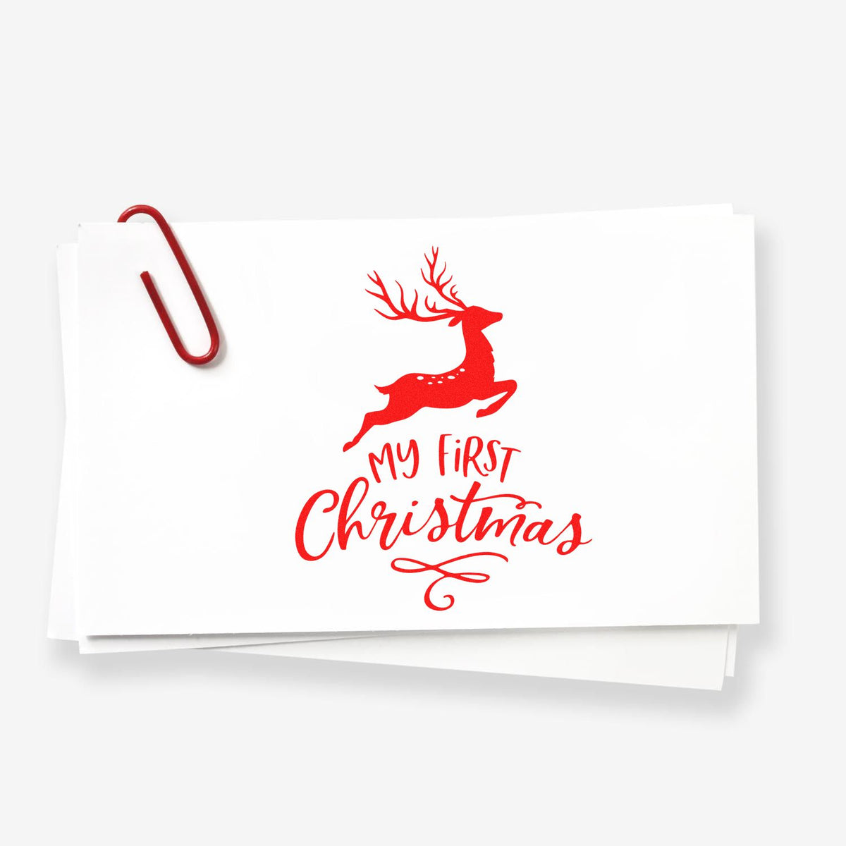 Red My First Christmas reindeer stamp seal on white card with a red paperclip.