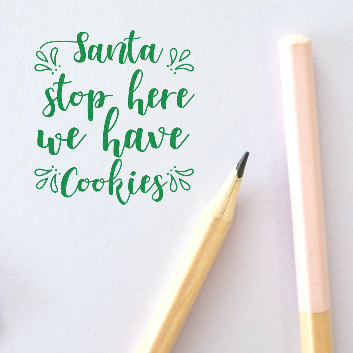 Green Santa stop here we have cookies stamp with decorative flourishes, beside a pencil and pink seal on white paper.
