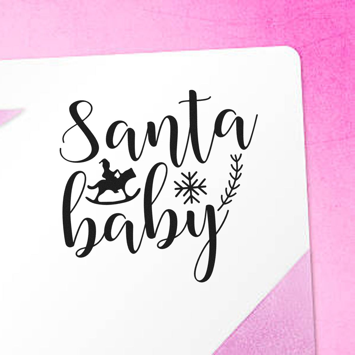 Black Santa baby stamp and seal design with rocking horse, snowflake, and branch on white paper against pink background