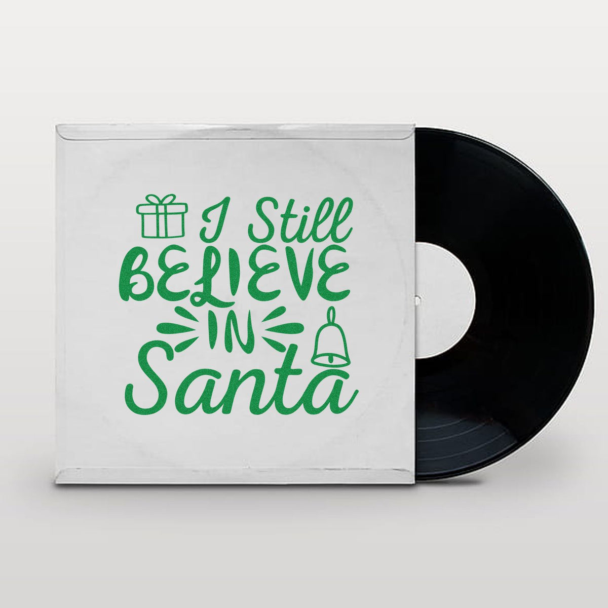 Green stamp-style I Still Believe in Santa design with gift and bell icons on a white sleeve, black vinyl record peeking out.