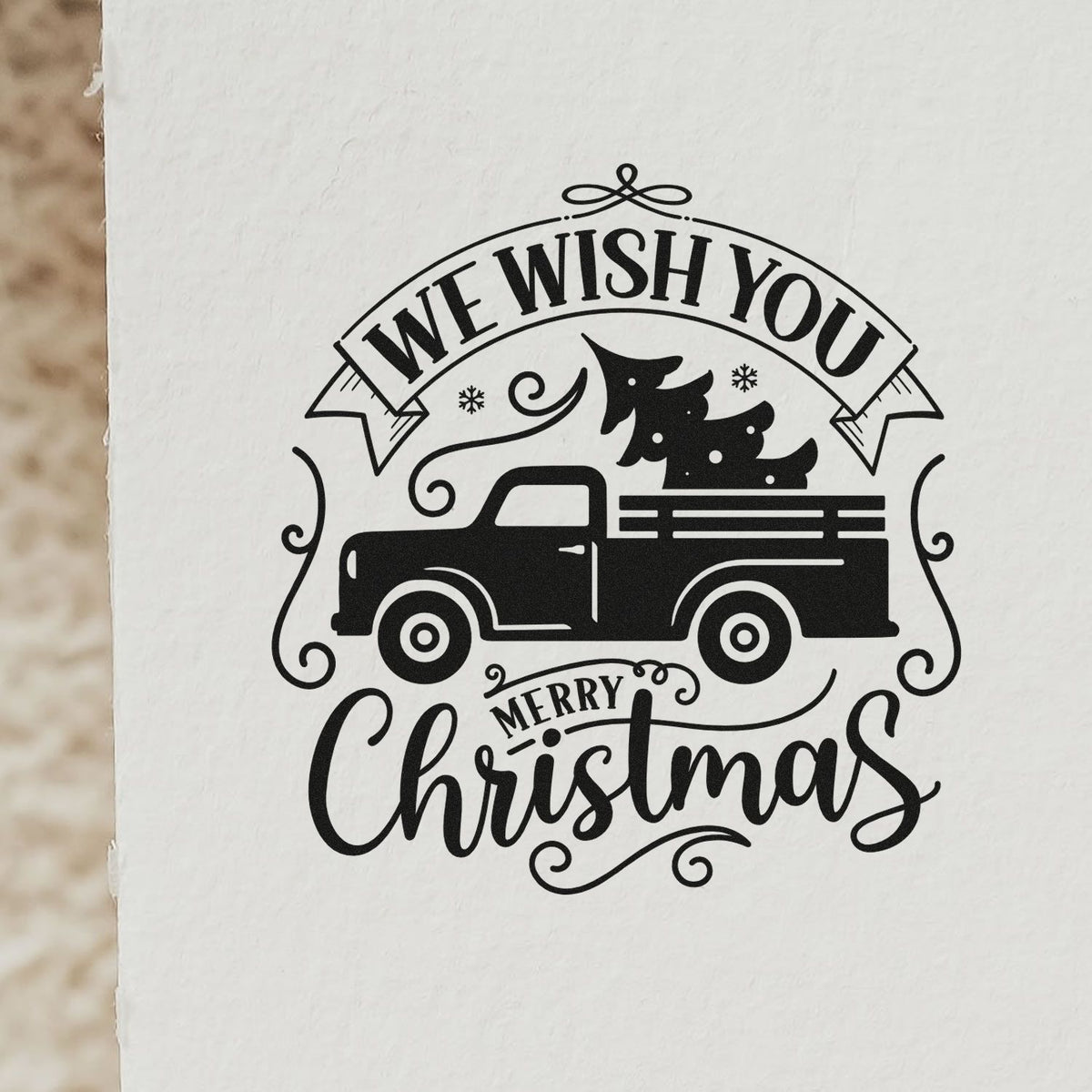 Black stamp and seal design with pickup truck, Christmas tree, and We Wish You Merry Christmas on white paper.