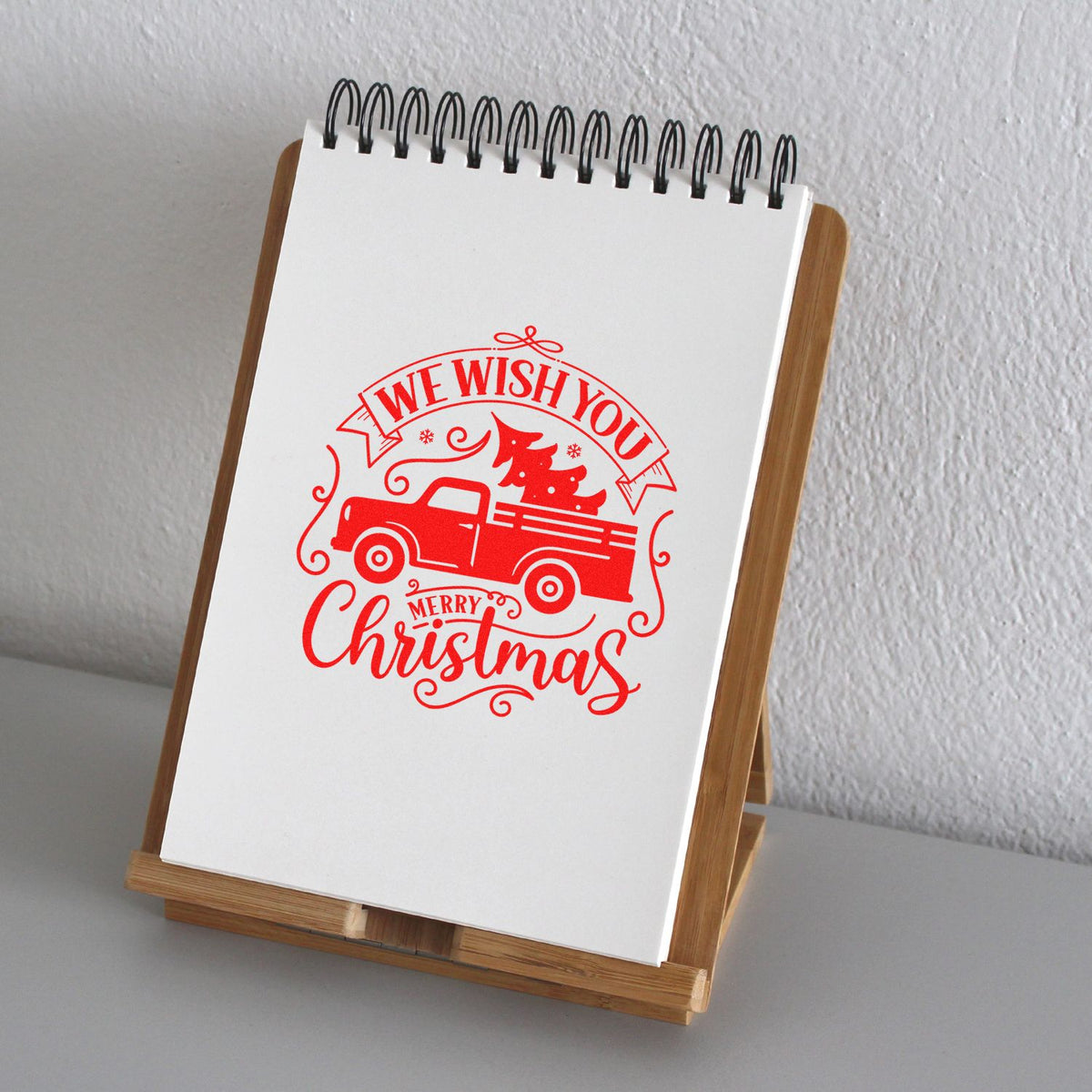 Red Christmas rubber stamp on white notepad, featuring a truck, tree and We Wish You Merry Christmas on a wooden stand.