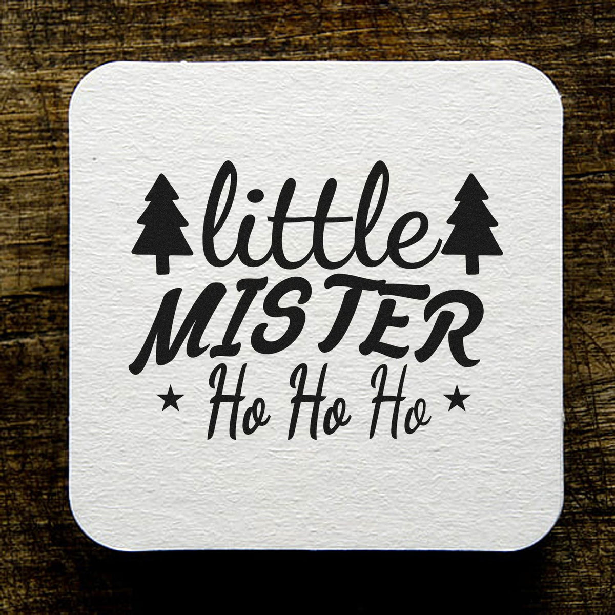 White square stamp seal with black little MISTER Ho Ho Ho text, pine trees and stars on a dark wood background.
