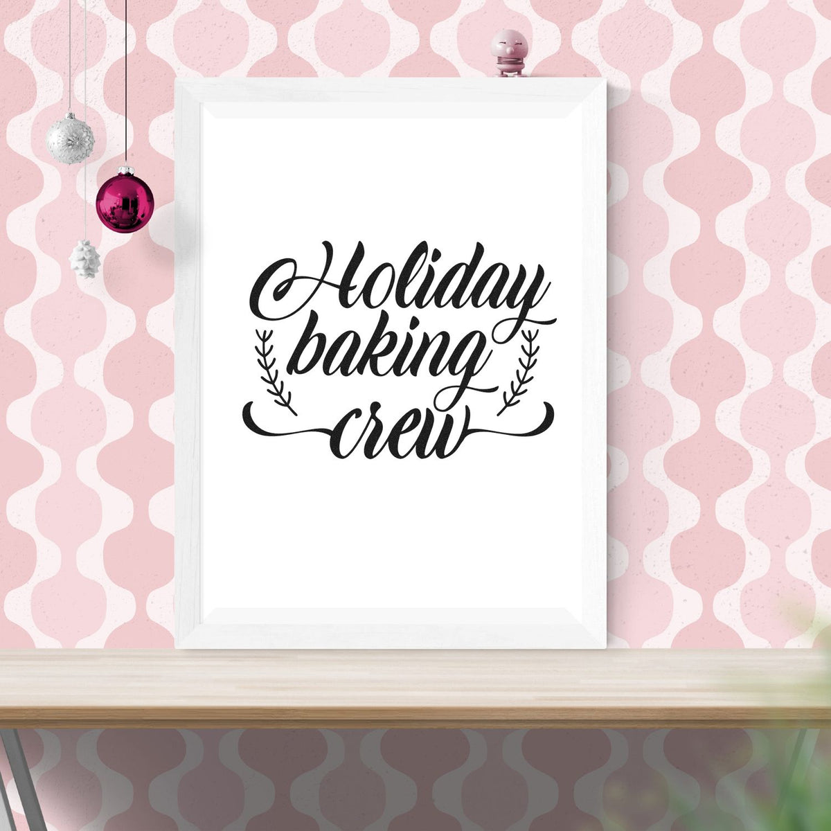 Holiday baking crew stamp design in black script on white frame, set against pink patterned background with hanging ornaments.