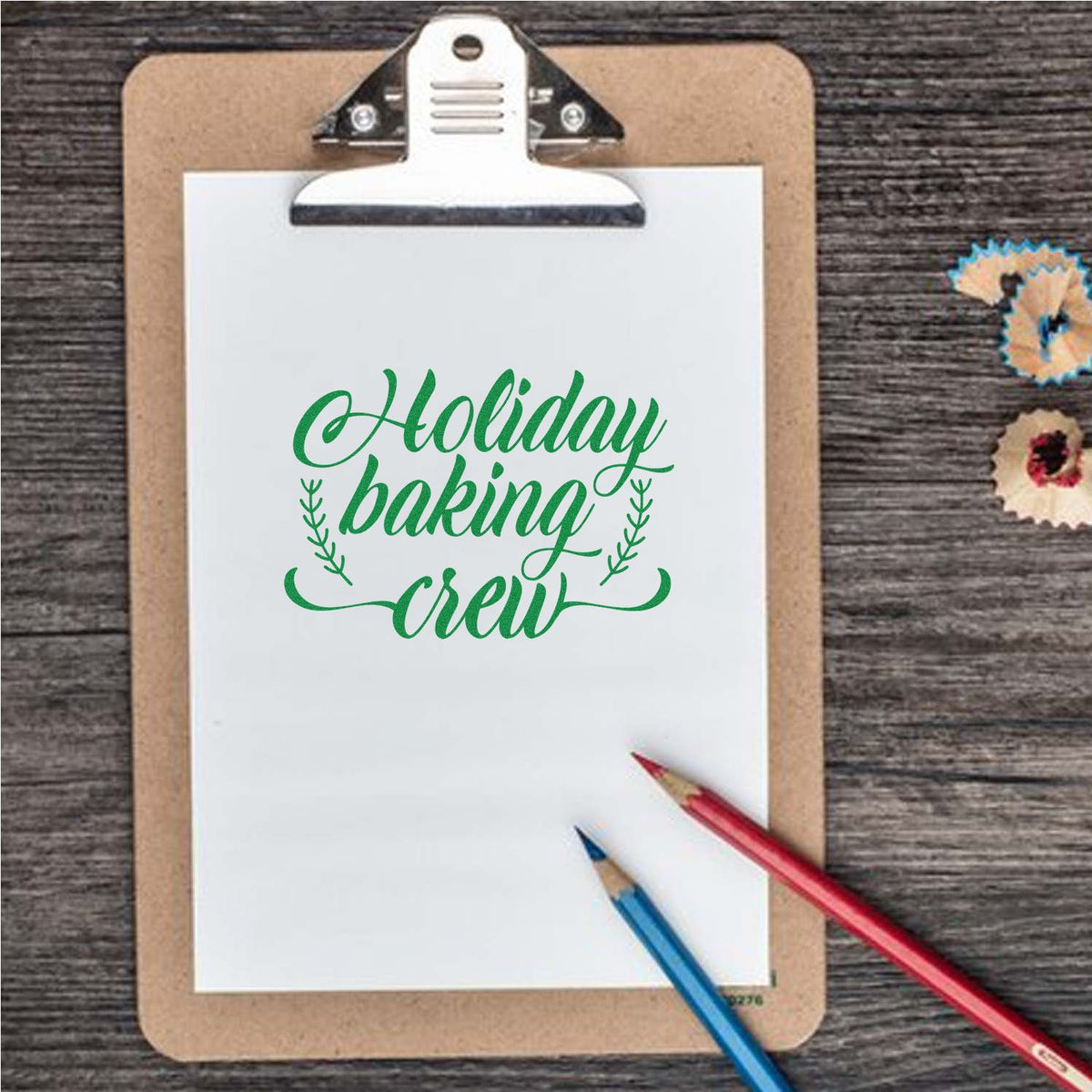 Green Holiday baking crew stamp on a clipboard, with pencils and colorful seal samples on a rustic wood background.