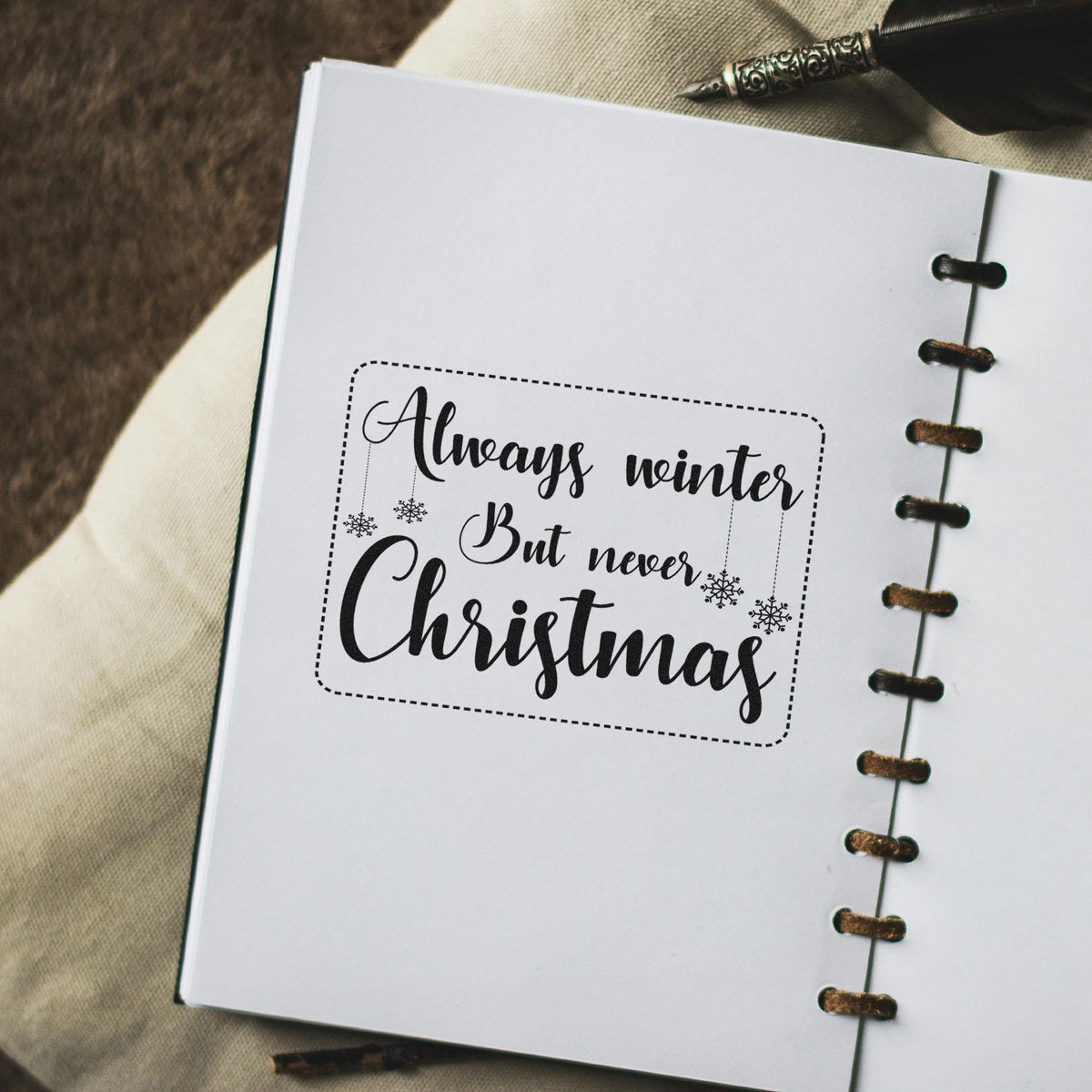 Black holiday stamp and seal on white paper: Always winter, but never Christmas with snowflakes and dotted border.