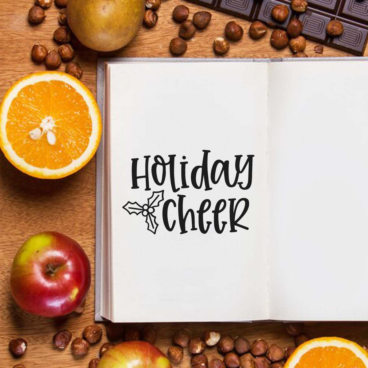 Holiday Cheer stamp and seal design in black with holly icon, on an open book with oranges, apples, and coffee beans.