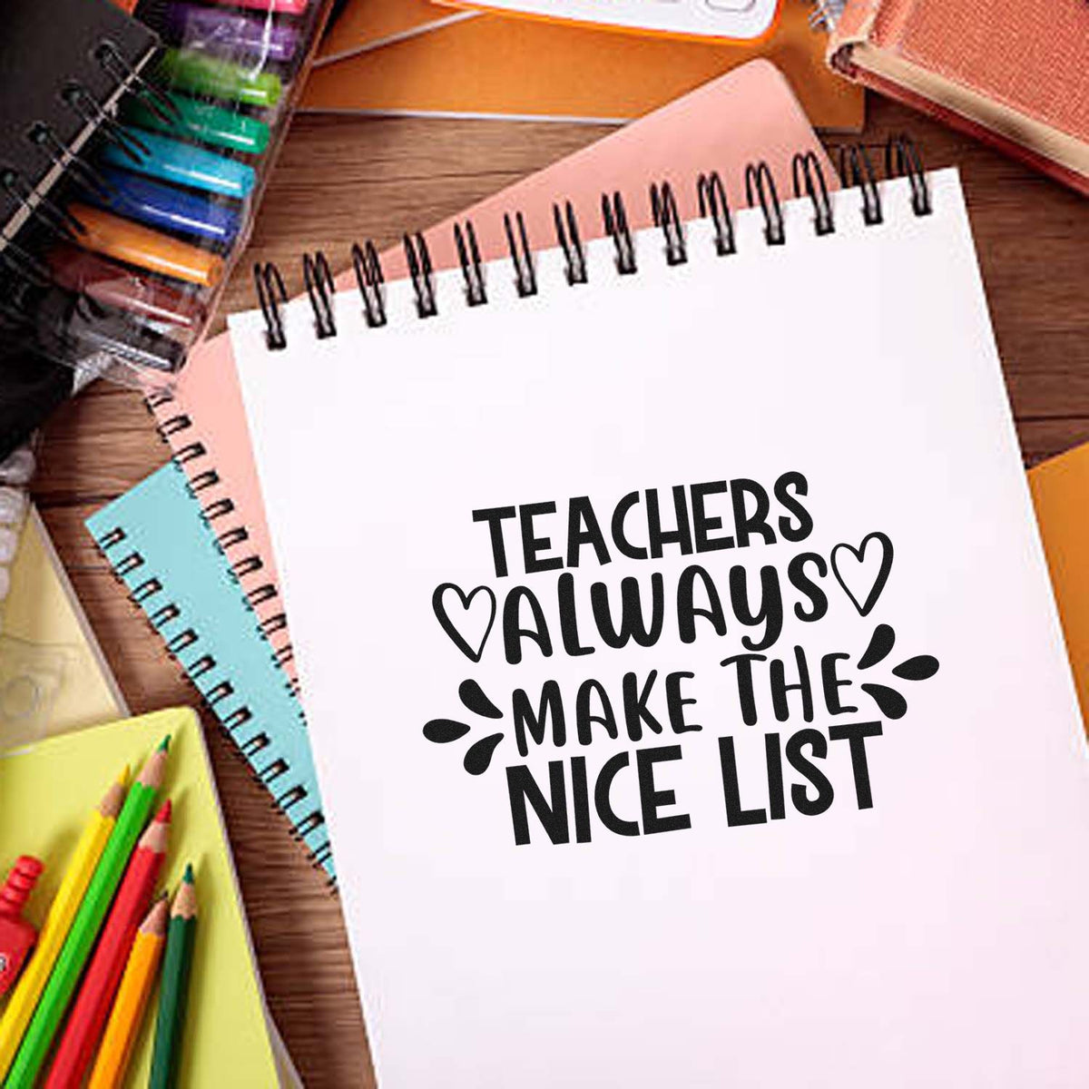 Teacher stamp and seal design on a white spiral notebook, with black text, hearts, and colorful pencils on a wooden desk.