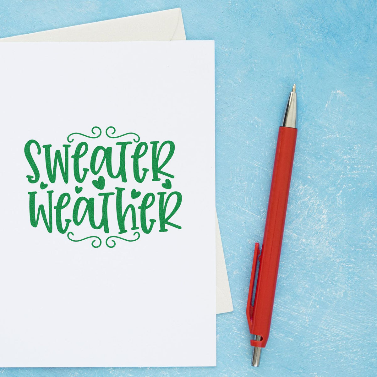 Green Sweater Weather stamp and seal on white card with red pen, set against a blue textured background.