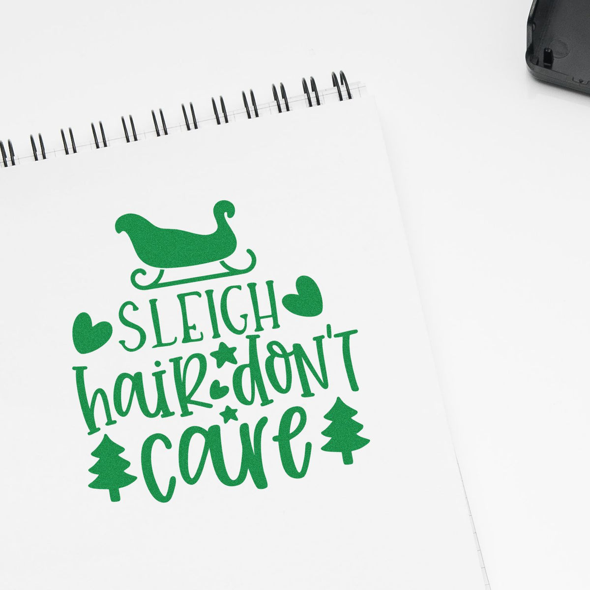 Green holiday stamp/seal on white spiral notebook reads Sleigh hair dont care with sleigh, hearts and trees.