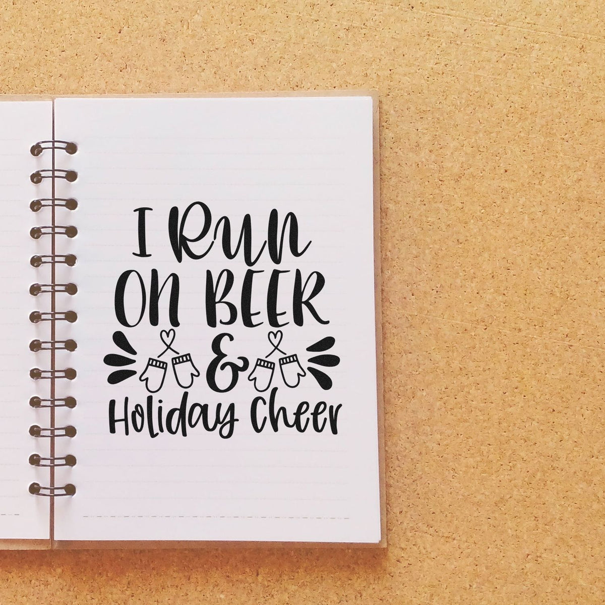 Black custom stamp reading I run on beer & holiday cheer with mitten accents on a white spiral notebook page.