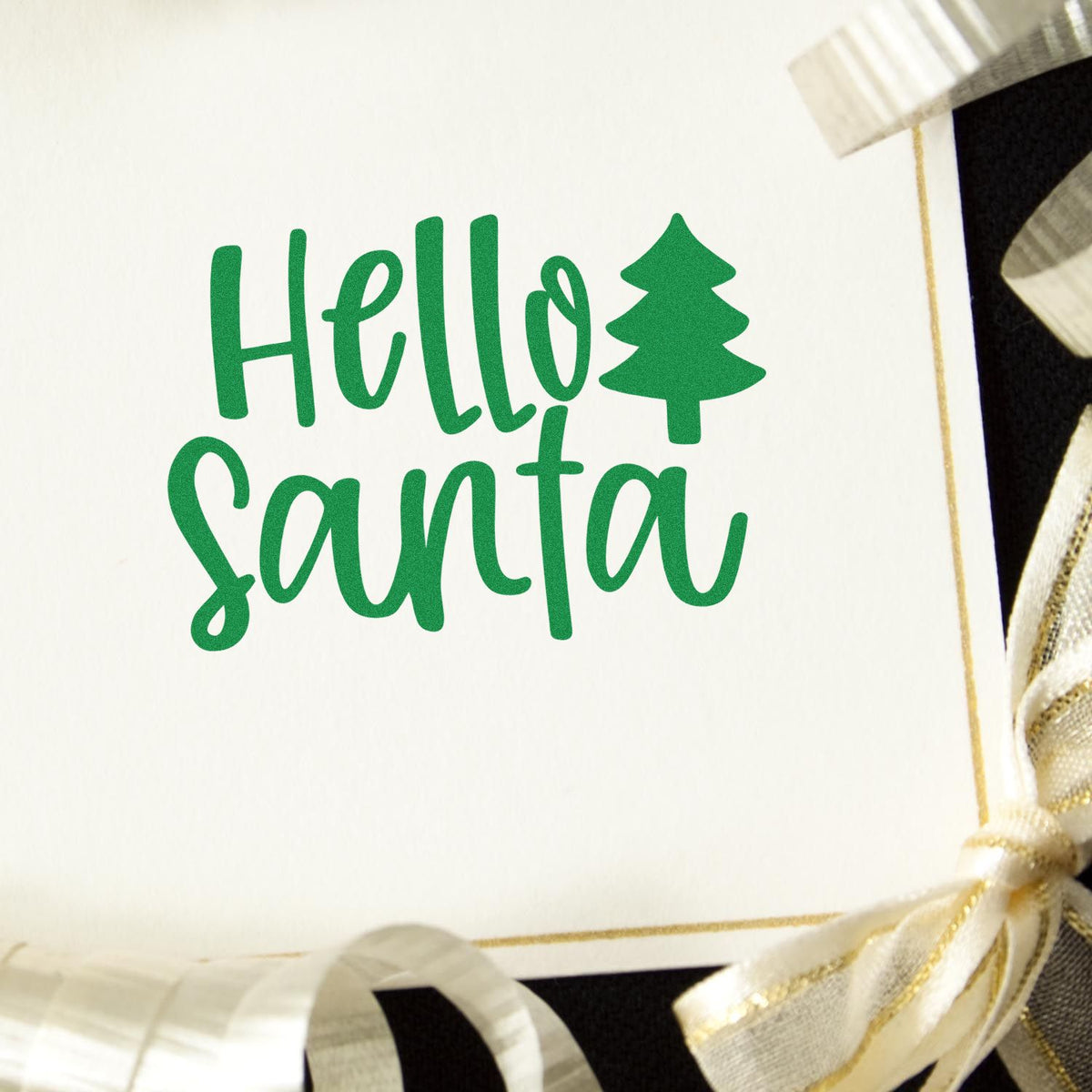 Green Hello Santa holiday stamp with pine tree icon on white card, trimmed with gold and cream ribbon bows.