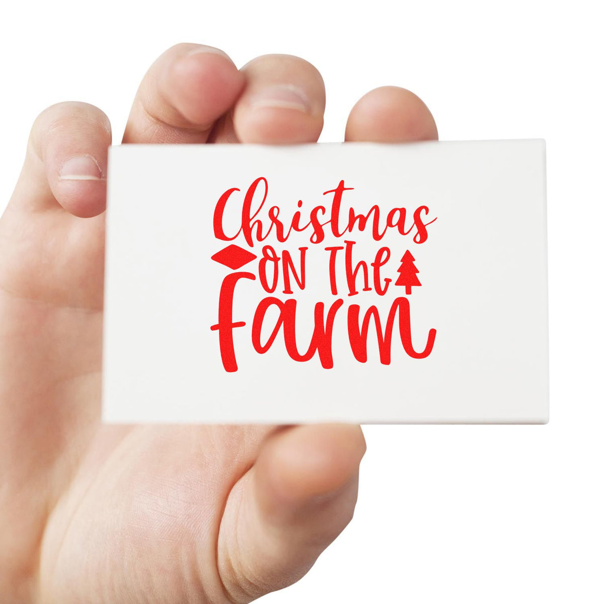 Hand holding white stamp seal with red Christmas on the Farm lettering and small red tree design.