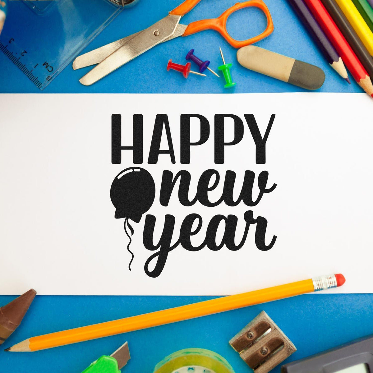 Black Happy New Year stamp and balloon seal on white paper, surrounded by colorful school supplies on a blue background.