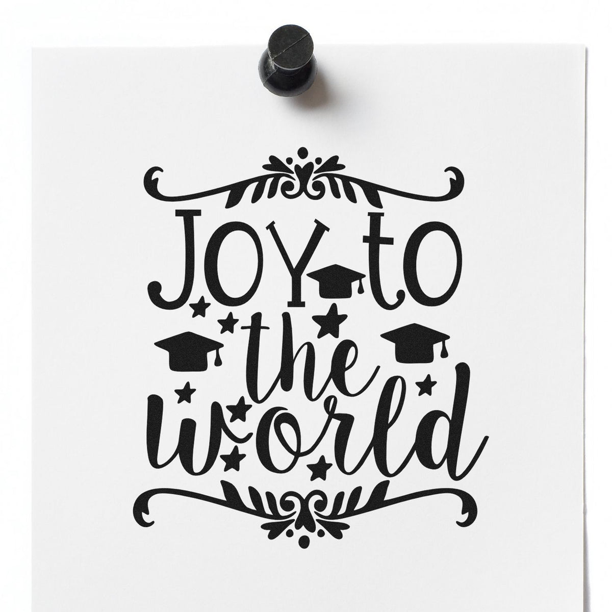 Black decorative stamp seal on white paper reading Joy to the world, with graduation caps, stars, and flourishes.