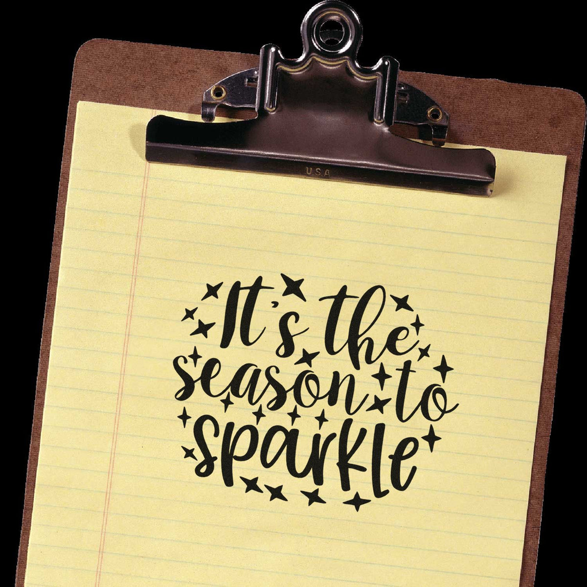 Custom stamp-and-seal design on yellow notepad reads Its the season to sparkle in black with star accents on a brown clipboard.