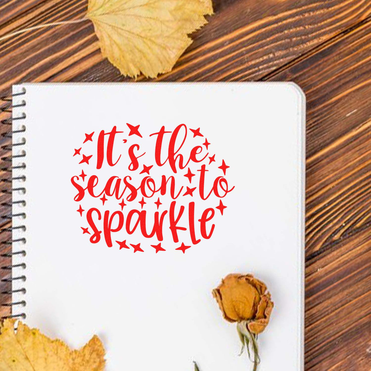 Red Its the season to sparkle stamp seal with stars on white spiral notebook, on rustic wood with autumn leaves.