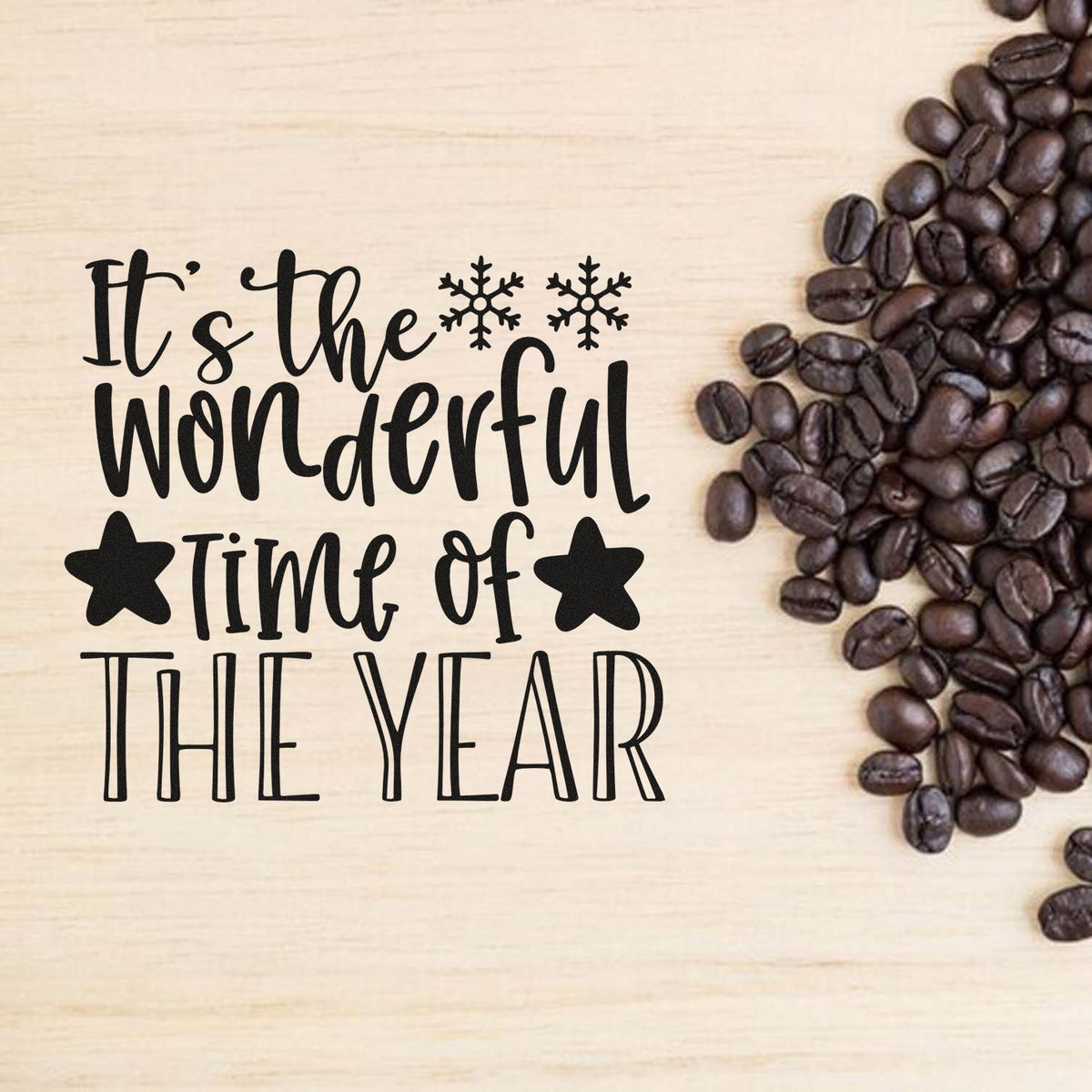 Black stamp and seal design reading Its the wonderful time of the year, with snowflakes, stars, and coffee beans on light wood.