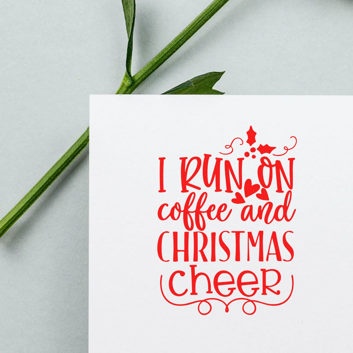 Red holiday stamp seal reading I run on coffee and Christmas cheer on white card, with green stem and pale gray background.