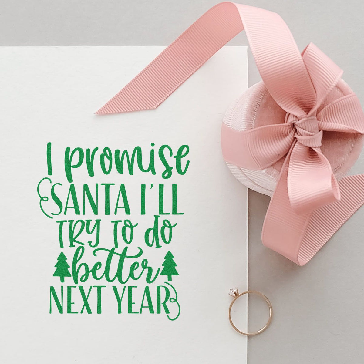 White holiday card stamp with green quote, pink ribbon bow seal, and gold ring seal on a soft gray background.