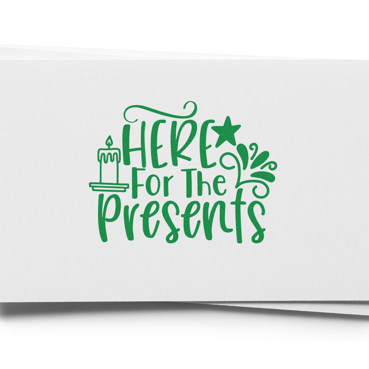 Green holiday stamp seal reading Here for the presents with a candle, star and swirls on white paper.