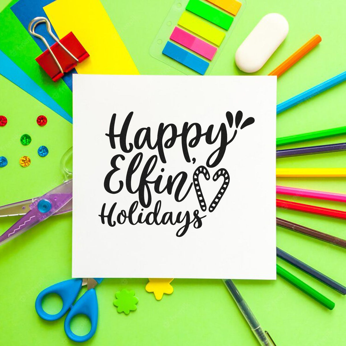 Black Happy, Elfin Holidays stamp and seal design on white card, framed by bright green, pink, blue, and yellow supplies.