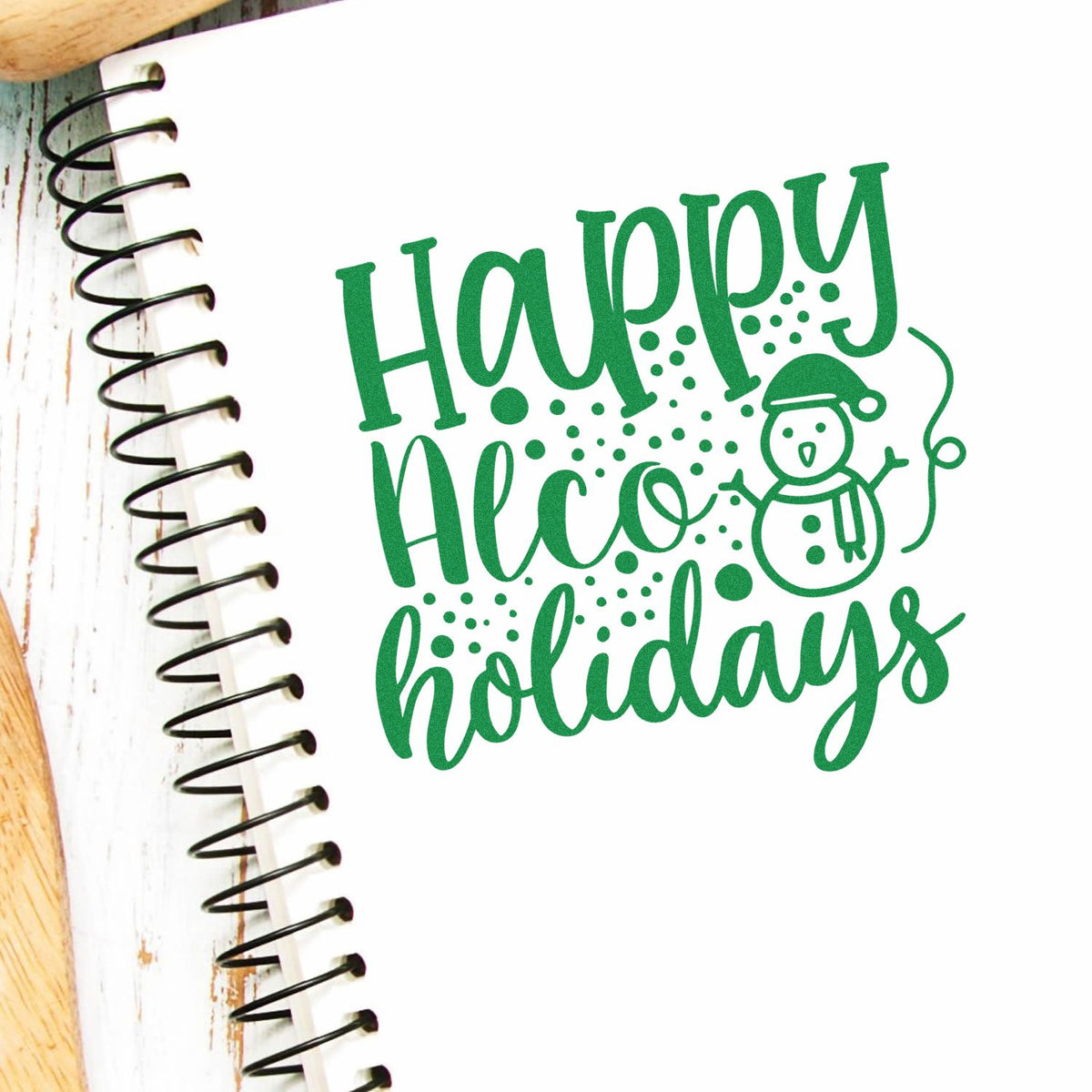 Green Happy Holidays stamp/seal with snowman and festive dots on a white notebook page.