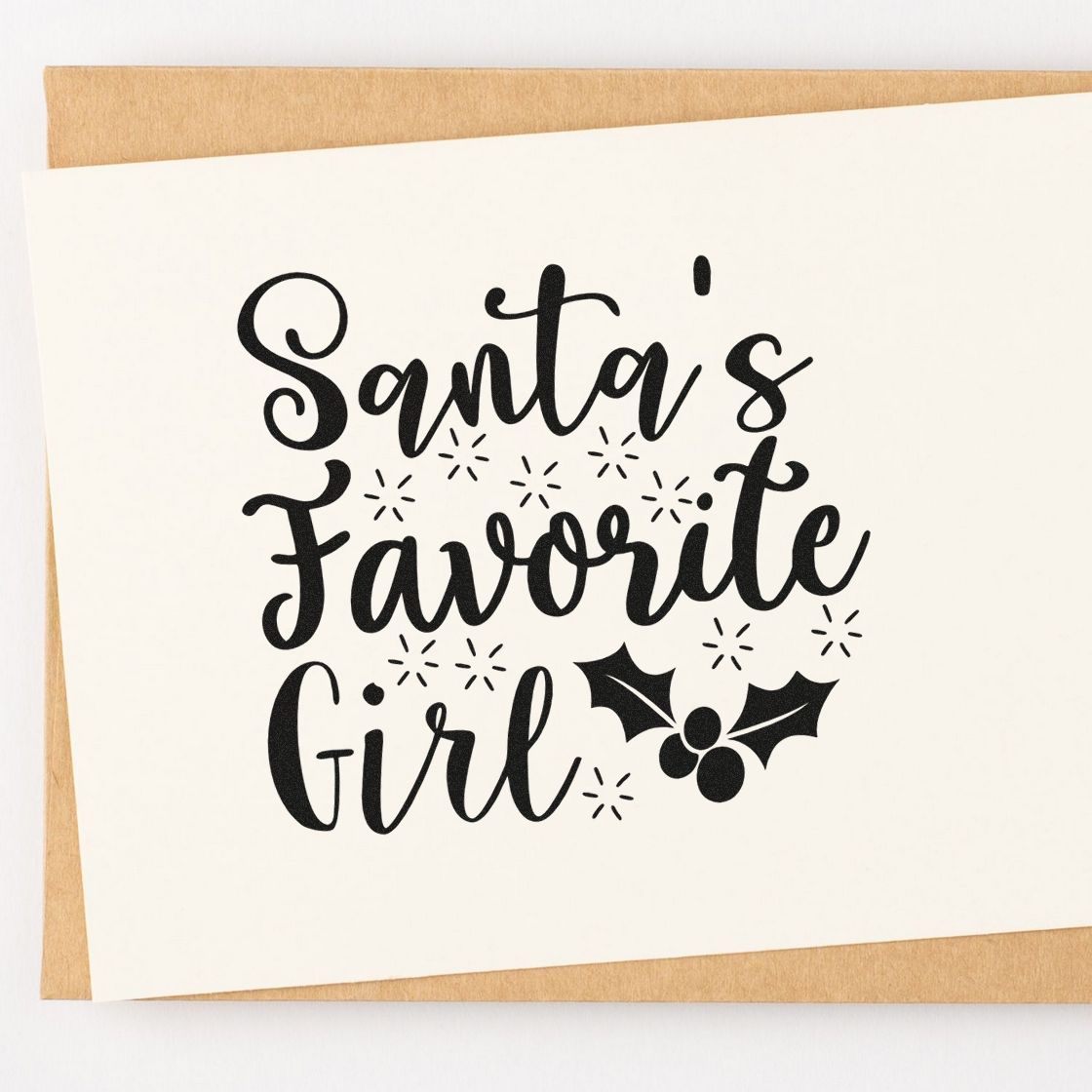 Black holiday stamp/seal reading Santas Favorite Girl with holly and starbursts on white cardstock.