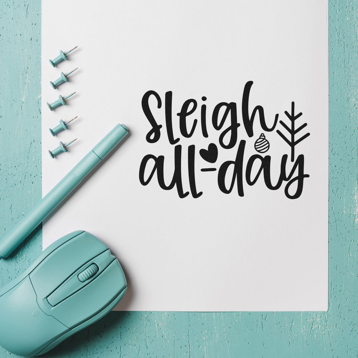 Mint stamp and seal kit with teal tools on white paper, creating black Sleigh all-day holiday lettering and festive icons