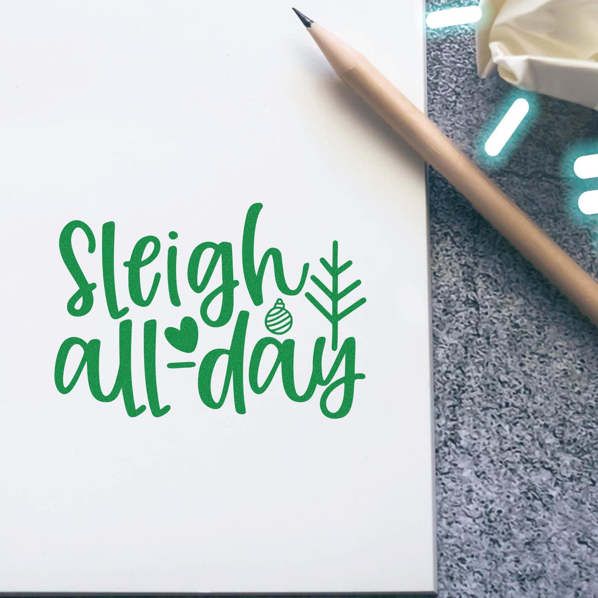 Green sleigh all-day stamp and seal design on white, with heart ornament, pine tree, and pencil.