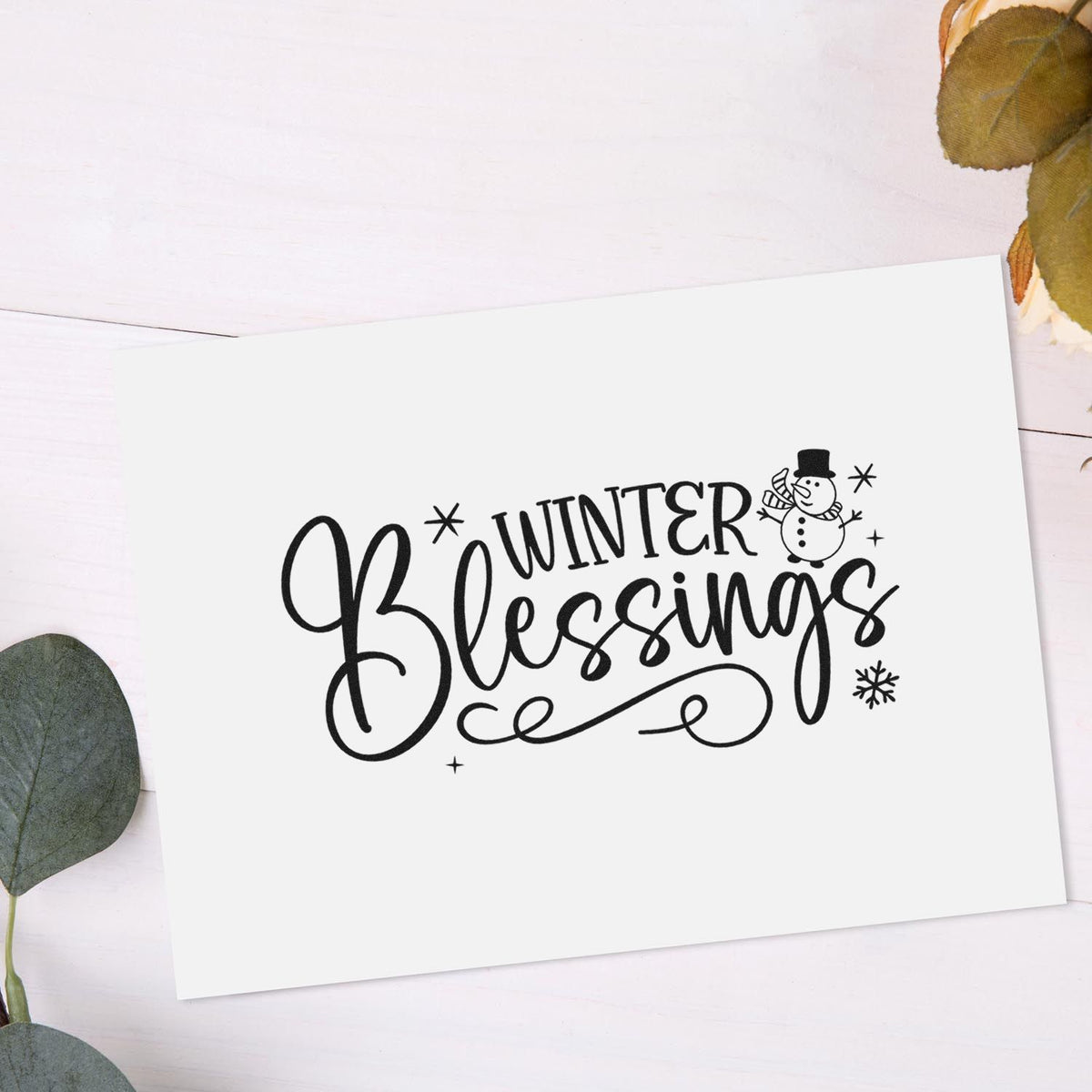 Black Winter Blessings stamp and seal on white card, with snowman, snowflakes and eucalyptus leaves.