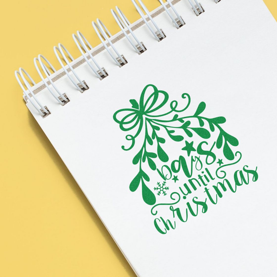 Green Christmas stamp and seal graphic on white spiral notebook, with bow, leaves, and until Christmas text on yellow background