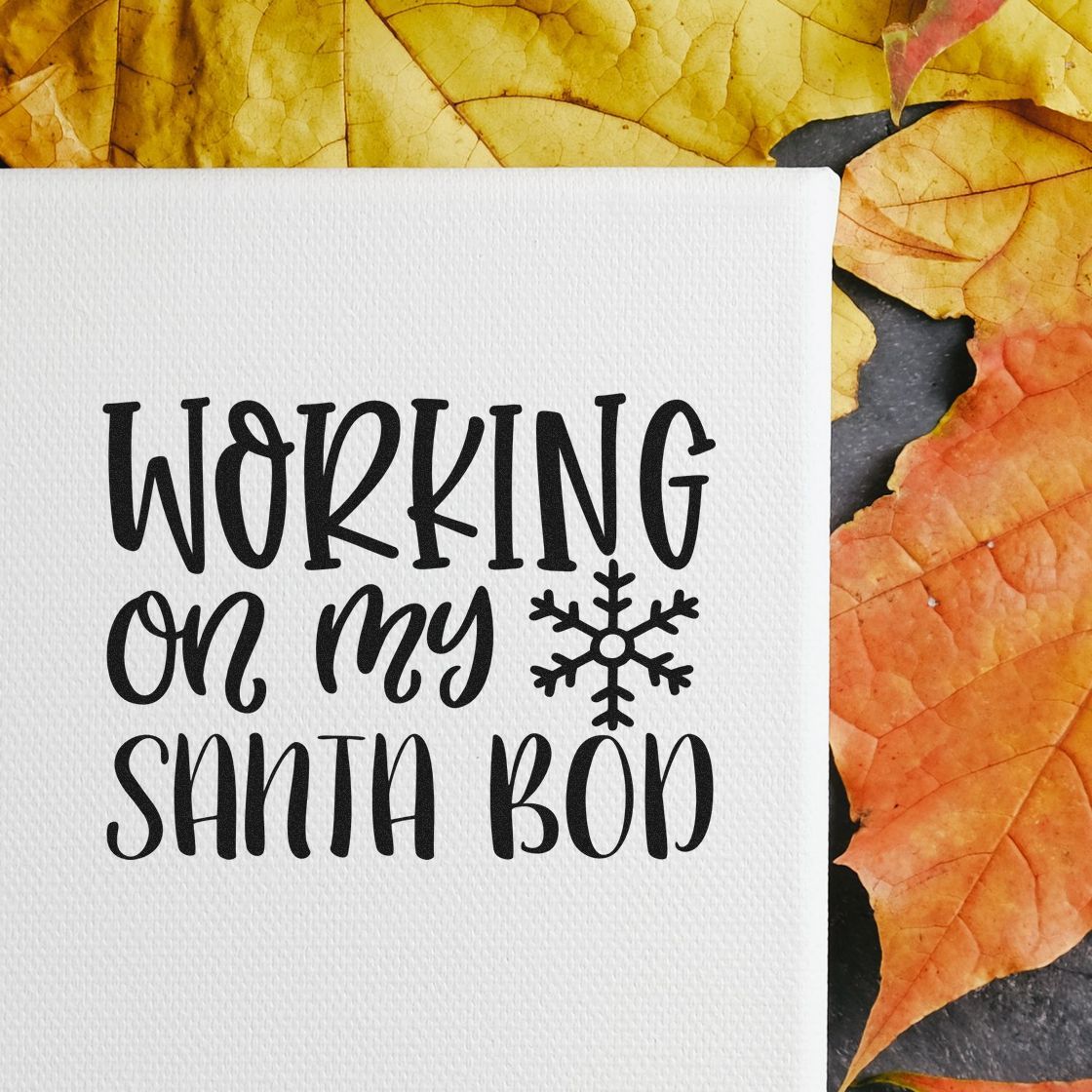 White textured card with black holiday stamp-and-seal reading Working on my Santa bod, plus a snowflake, framed by yellow and orange leaves.