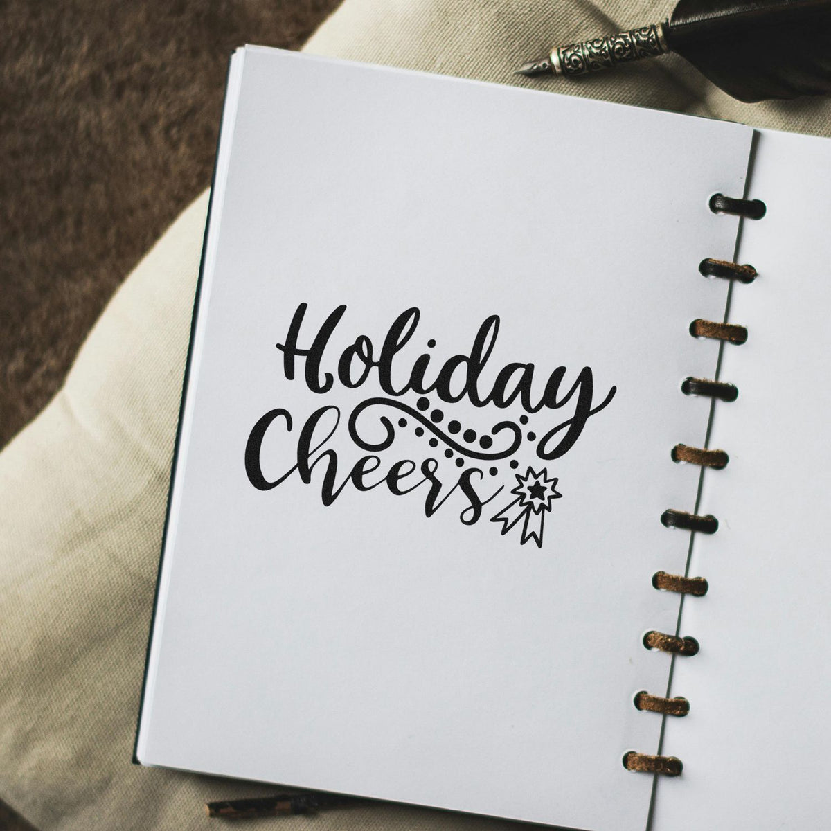 Black Holiday Cheers stamp with decorative seal on white notebook page, accented by brown lacing and pen.