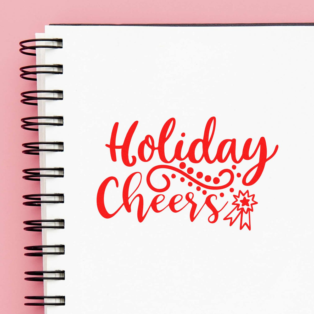 Red Holiday Cheers stamp and seal design on white spiral notebook, with decorative ribbon seal and pink background.