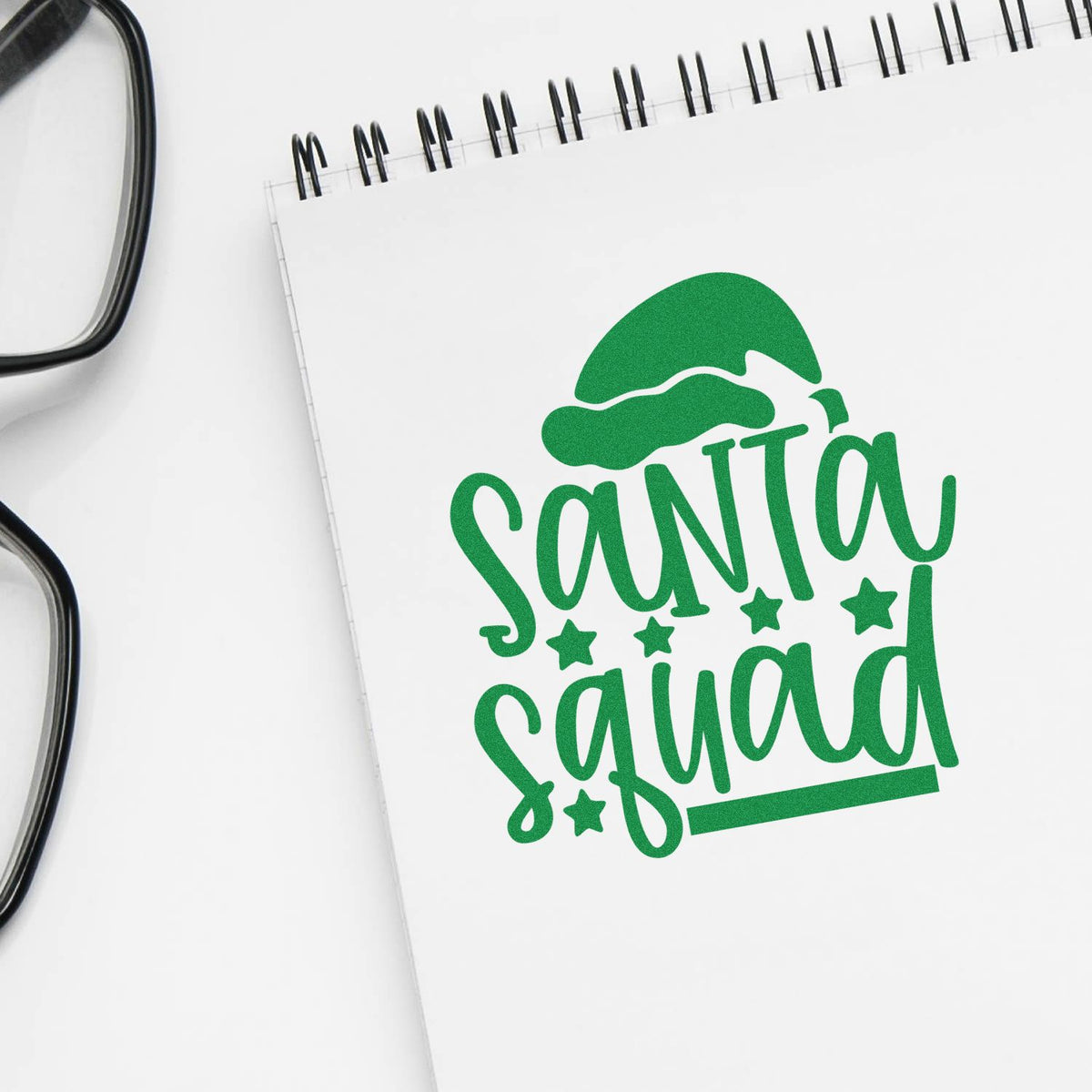 Green Santa Squad stamp and seal design with Santa hat and stars on a white spiral notebook.