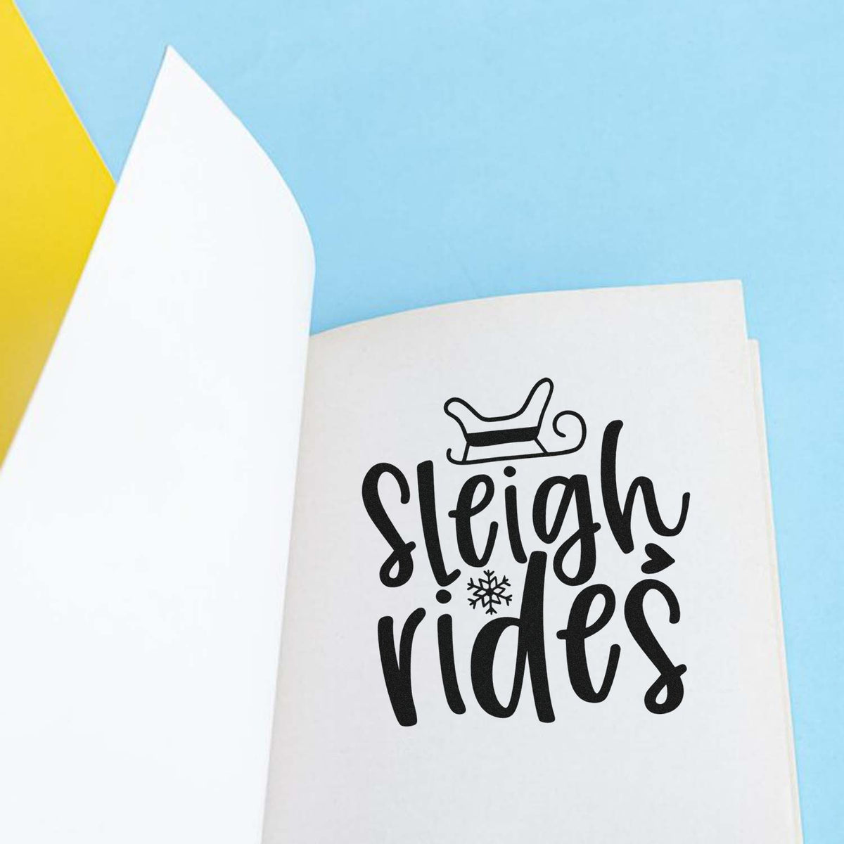 Black sleigh rides stamp and seal design with sleigh icon and snowflake on white paper, on a light blue background.