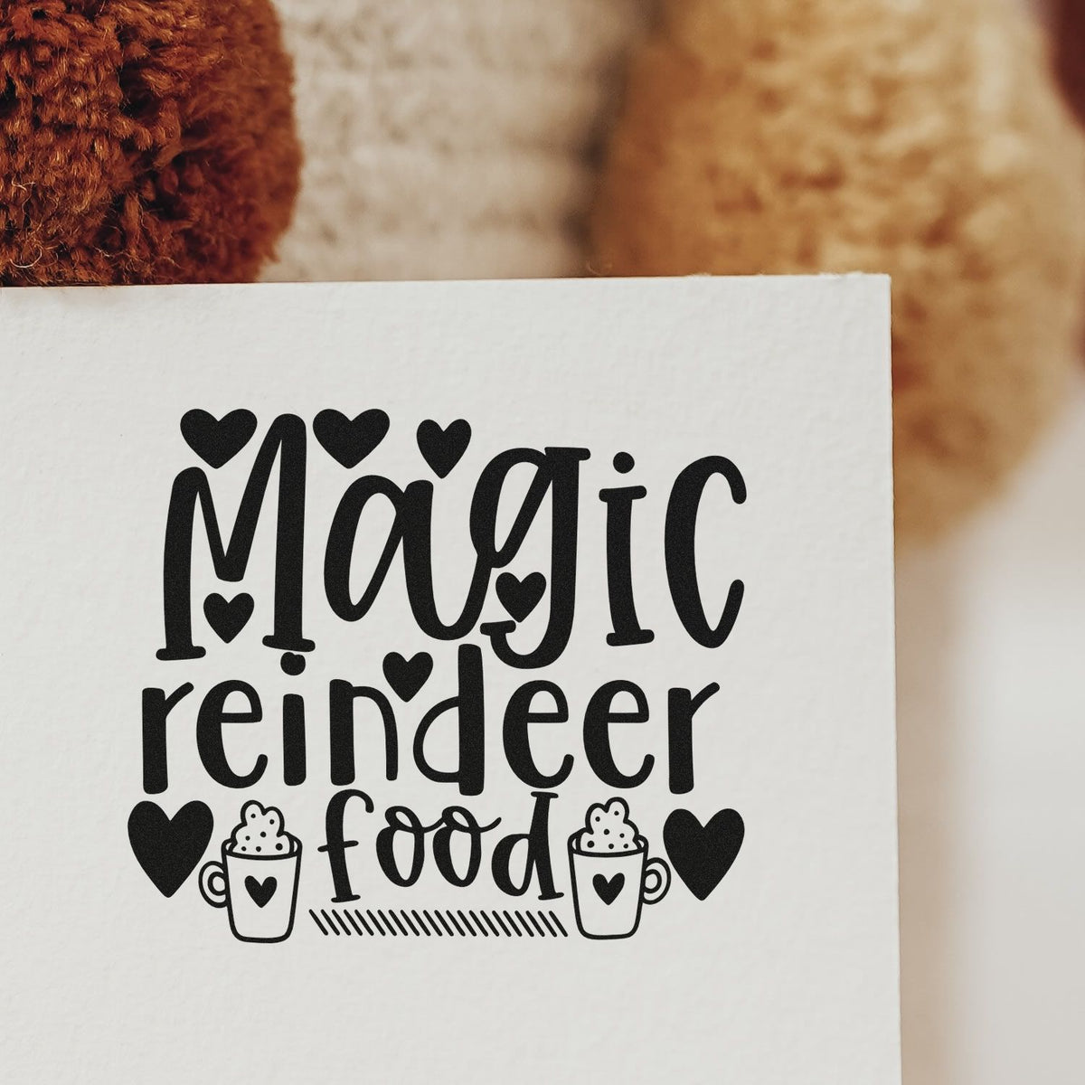 Black stamp and seal design reading Magic reindeer food with hearts and mug icons on white paper.