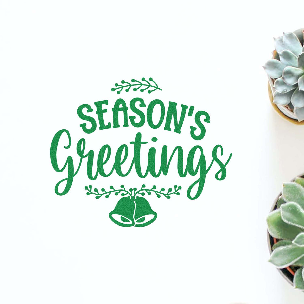 Green Seasons Greetings stamp and seal with bells and leaves on white, beside succulents.